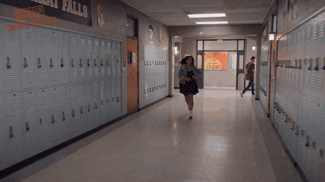 a girl in a dress is running down a hallway with lockers in the background