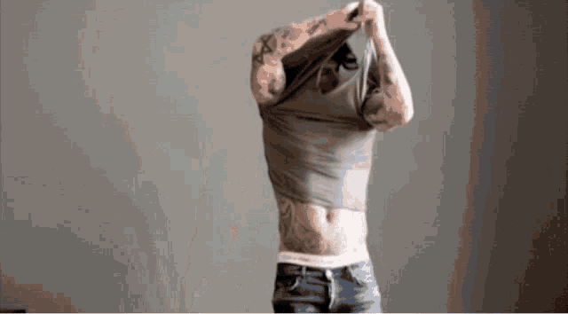 a man with tattoos on his arms and torso is taking off his shirt