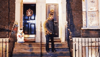a man is standing on the steps of a house with a wreath on the door .