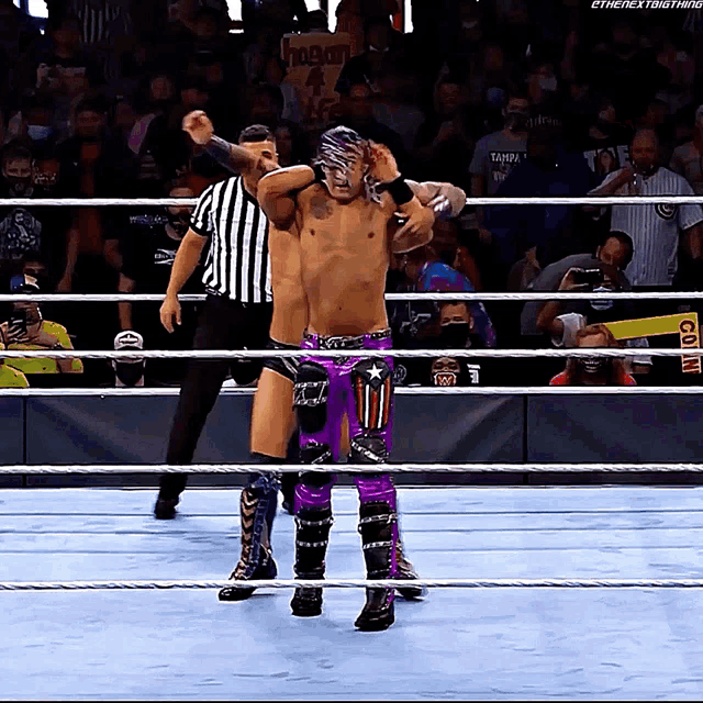 a wrestler in a purple outfit is standing in a ring with a referee