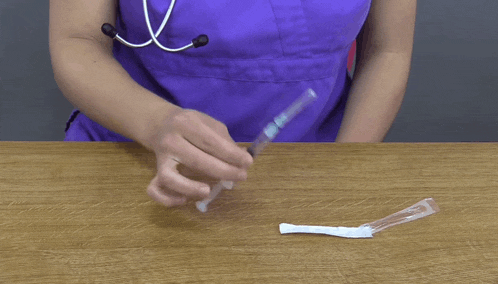 a woman in a purple scrub is holding a syringe on a wooden table