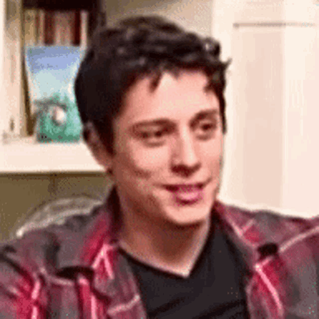 a young man in a plaid shirt and black shirt is sitting on a couch .