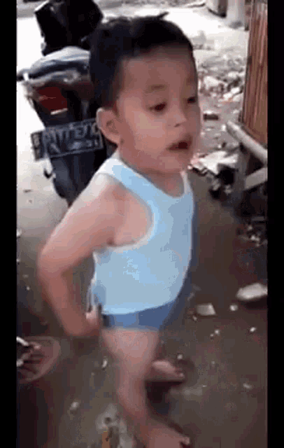 a young boy in a blue tank top and blue shorts is standing on a street .