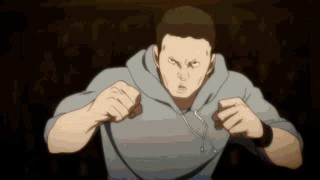 a man in a grey hoodie is standing in a dark room with his fist in the air