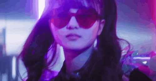 a close up of a woman wearing sunglasses in a dark room with purple lights .