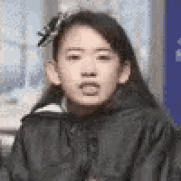 a woman in a black jacket is making a funny face while sitting in front of a window .