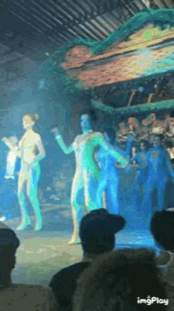 a group of people are dancing on a stage while a crowd watches .