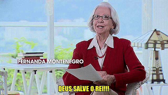 an elderly woman in a red sweater holds a piece of paper and says deus salve o rei !!!
