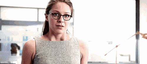 a woman wearing glasses and a grey dress is standing in front of a window .