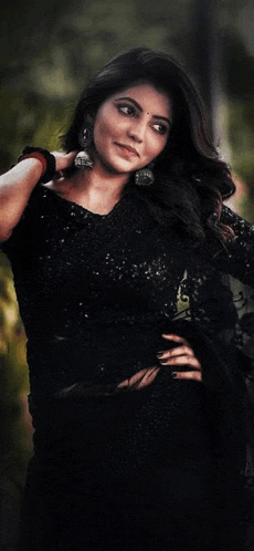 a woman wearing a black dress and earrings is standing in front of a tree .