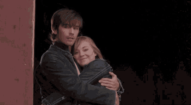 a man and a woman hugging each other in front of a red wall