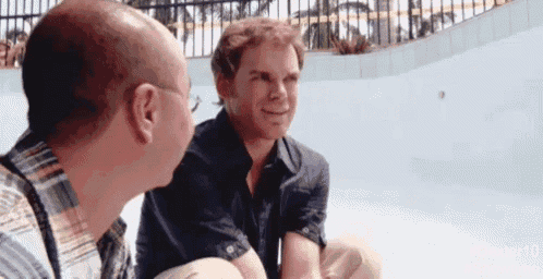 two men are sitting next to each other in front of a pool and talking .