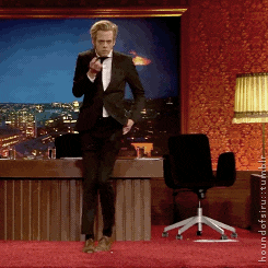 a man in a tuxedo is standing on a red carpet in front of a desk