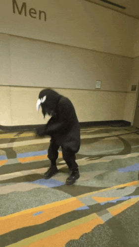 a person in a black costume is dancing in a hallway with the word men on the wall behind them