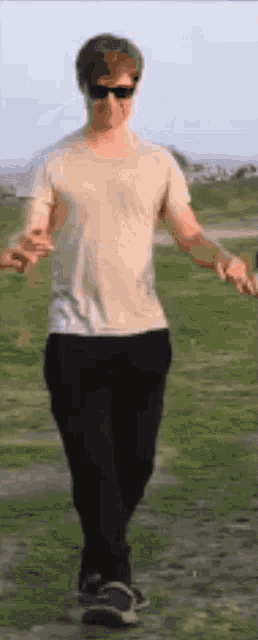 a man in a white shirt and black pants is walking on a grassy field .