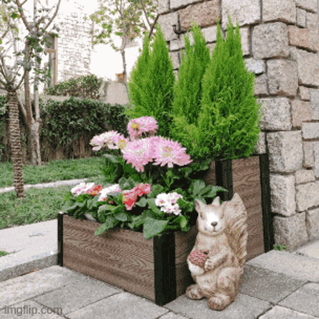 a squirrel statue sits next to a wooden planter filled with flowers and plants