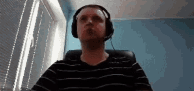 a man wearing headphones and a headset is sitting in a chair in front of a window .