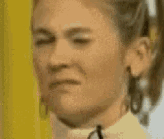 a close up of a woman 's face with a ponytail and earrings making a funny face .