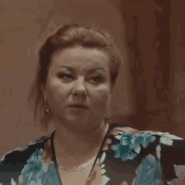 a woman wearing a floral dress and a necklace is making a funny face .