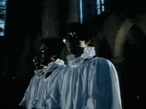 a group of men in white robes are singing in a dark room
