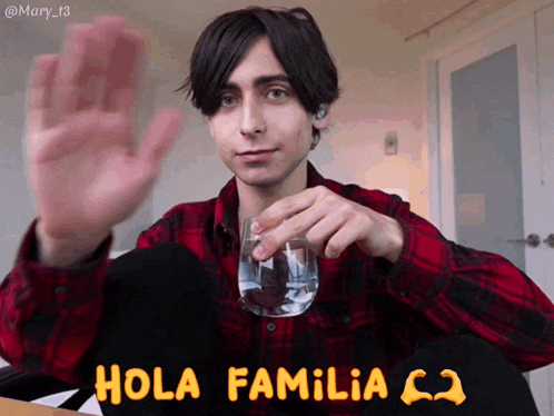 a young man in a plaid shirt is holding a glass of water and says hola familia