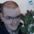 a man wearing glasses is sitting in front of a vase of flowers and smiling .