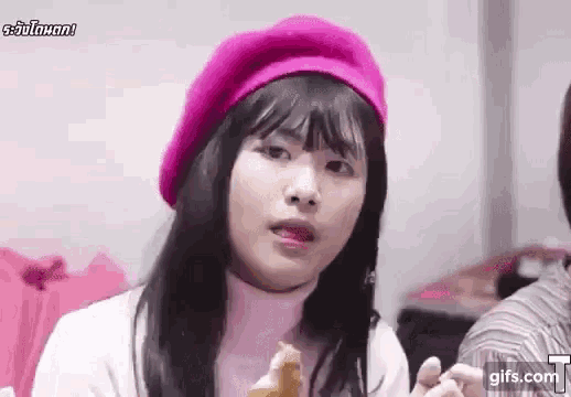 a woman wearing a pink beret and a white sweater is eating a sandwich .