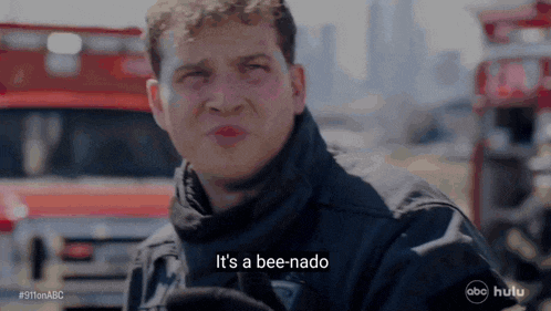 a man in a black jacket says it 's a bee-nado in front of a fire truck