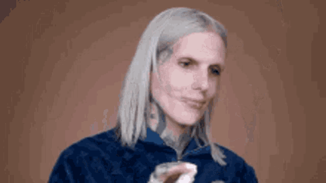 a woman with gray hair and a tattoo on her neck is wearing a blue jacket and holding a cup .