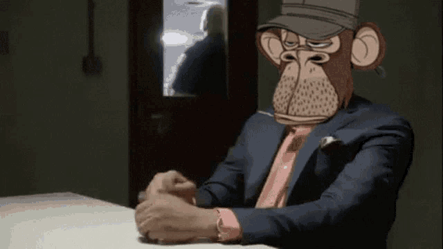 a man with a monkey mask on his face is sitting at a table with his hands folded .