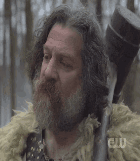 a man with long hair and a beard is holding a spear and the letters cw are on the bottom