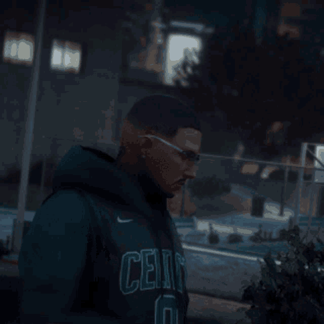 a man wearing a celtics sweatshirt is standing in front of a building