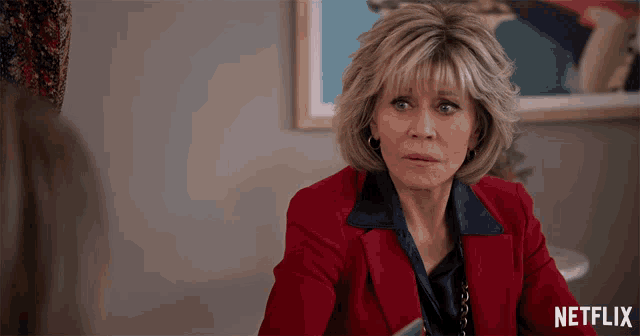 a woman in a red jacket is sitting in front of a netflix ad