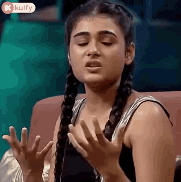 a young woman with braids is sitting on a couch with her hands outstretched .