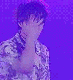 a man in a floral shirt is covering his face with his hand while standing in front of a purple background .