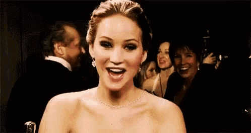 a woman wearing a necklace and earrings is smiling while standing in a crowd of people .