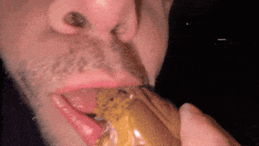 a man with a beard is eating a piece of food with his tongue out