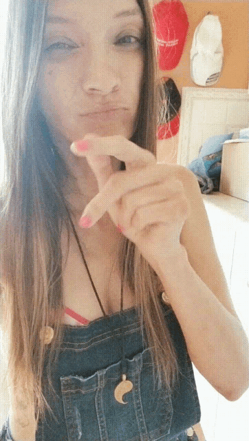 a girl wearing overalls is making a funny face with her fingers