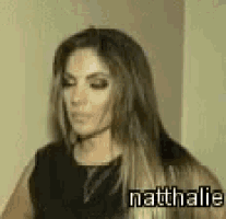 a woman with long hair is standing next to a wall and the name natthalie is on the bottom of the image .