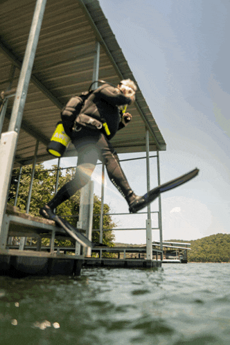 a scuba diver is jumping into the water while wearing a black wetsuit that says aqualung on the bottom