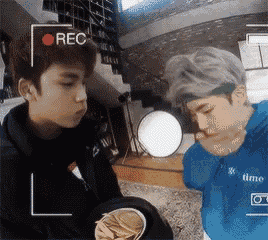 a couple of young men are standing next to each other in a room eating chips .
