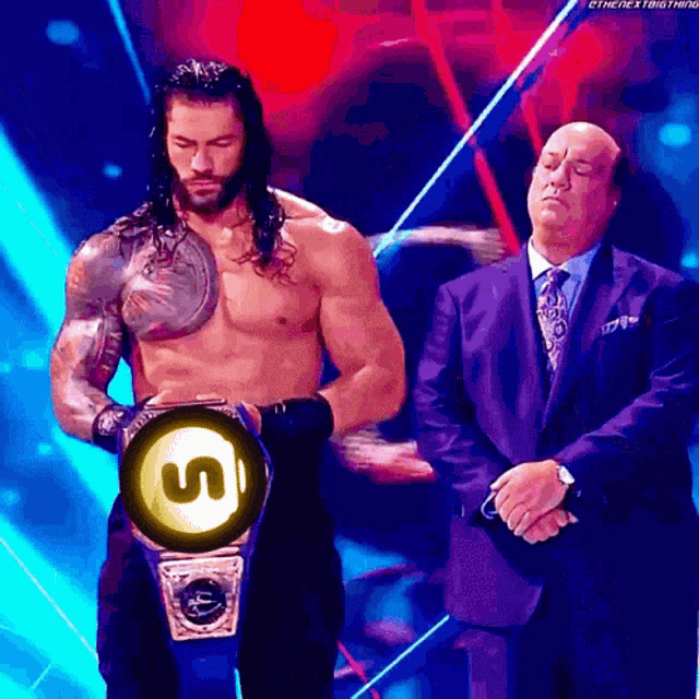 a man in a suit and tie stands next to a shirtless wrestler holding a championship belt with the letter s on it