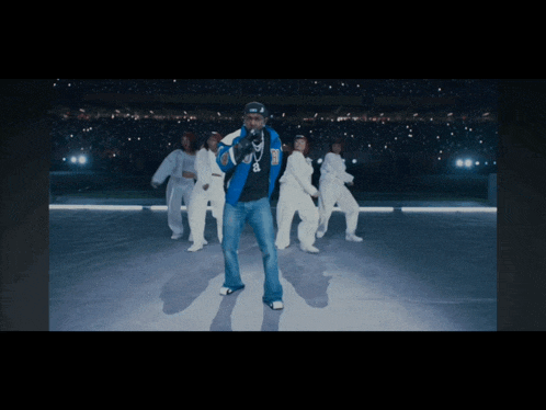 a man in a blue jacket stands in front of a group of dancers