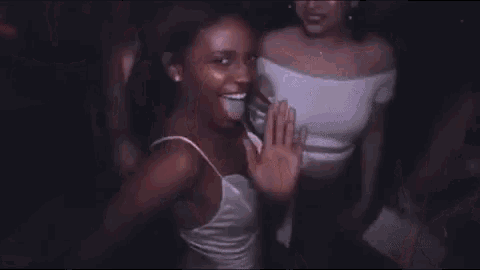 a woman is dancing in a club with her arms outstretched while another woman looks on .