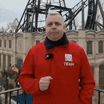 a man wearing a red team jacket stands in front of a roller coaster .