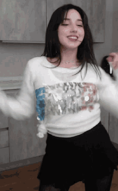 a woman in a white sweater and black skirt is dancing in a kitchen