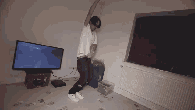 a man in a white shirt is dancing in a room with a tv and a crate of coca cola