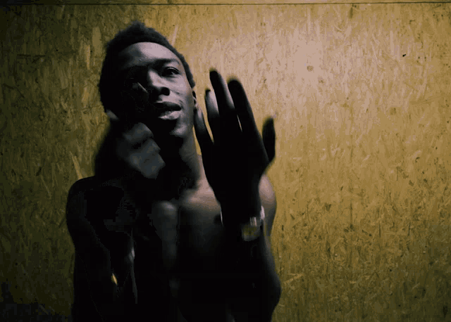 a shirtless man is waving his hand in front of a yellow wall
