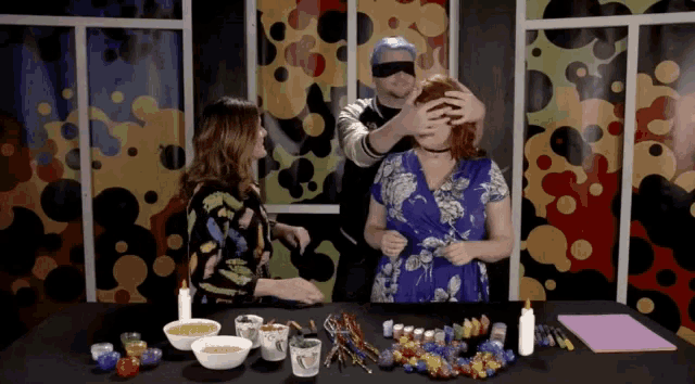 a man covering a woman 's eyes while another woman looks on