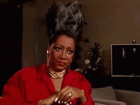 a woman in a red shirt and gold jewelry is sitting on a couch in a living room .